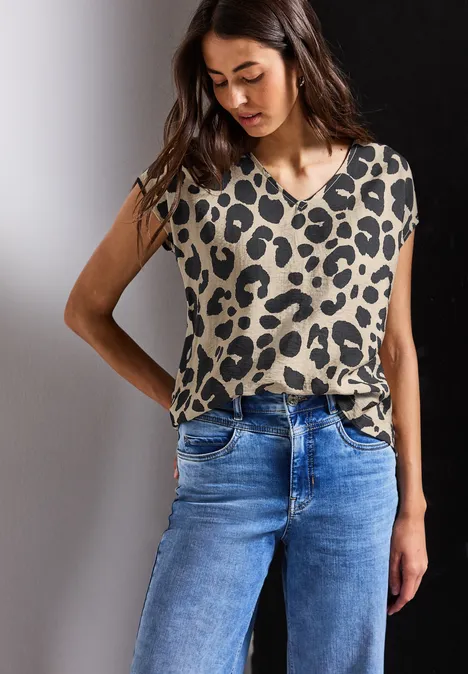 Frau mit Leopardenmuster-Shirt und blauer Jeans steht vor zweifarbigem Hintergrund.